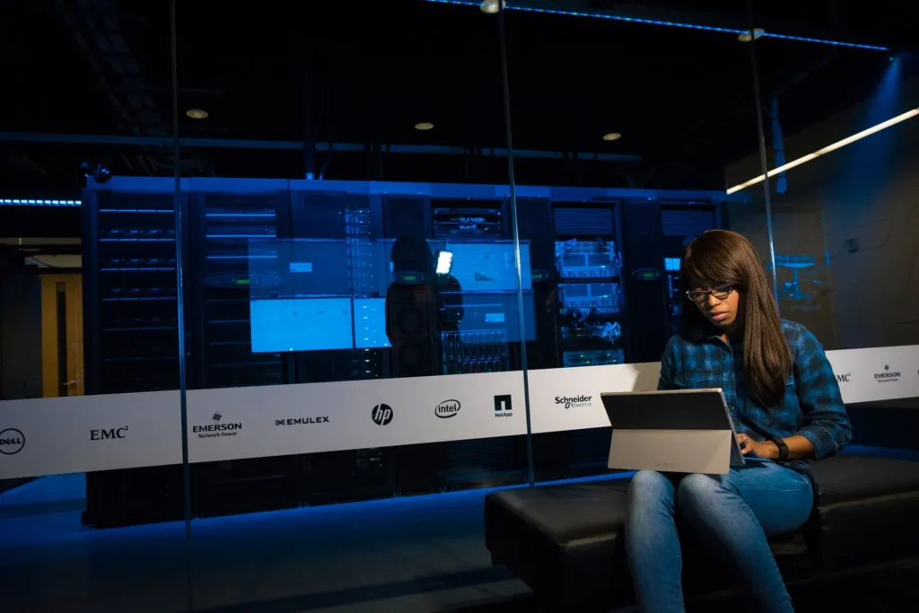 Woman working on a laptop in a data hall lined with equipment